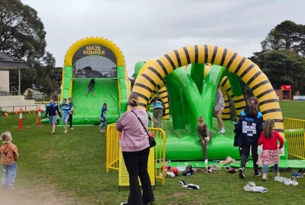 Children playing on an inflatable "Maze Runner" obstacle course in a grassy field.