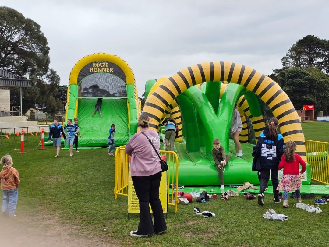 Children playing on an inflatable "Maze Runner" obstacle course in a grassy field.