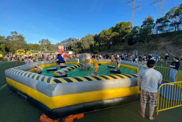 Children playing on an inflatable ride at an outdoor event, surrounded by crowds.