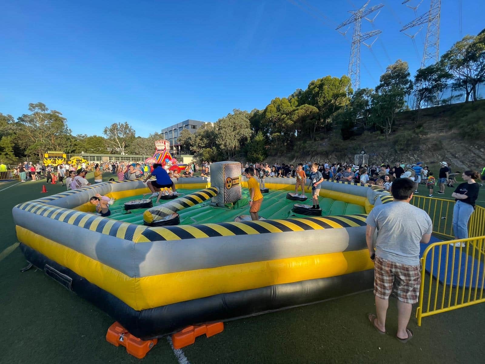 Children playing on an inflatable ride at an outdoor event, surrounded by crowds.